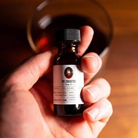 dr. squatch sandalwood bourbon cologne being held in front of a glass on a wooden table