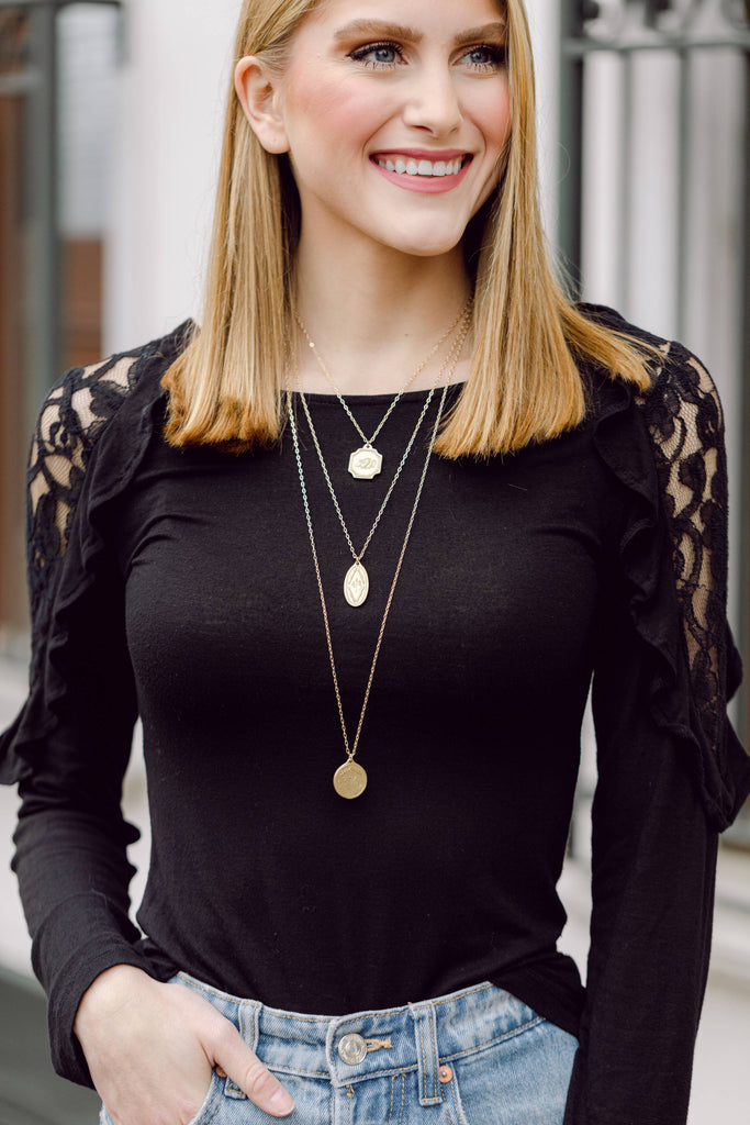 person wearing multiple necklaces in front of a gate