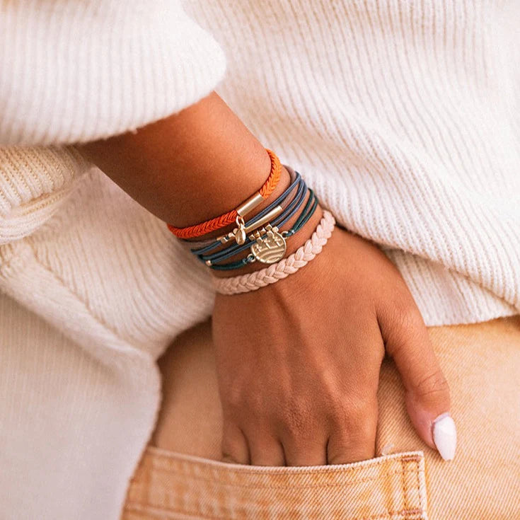 Hand wearing multiple bracelets with a neutral background