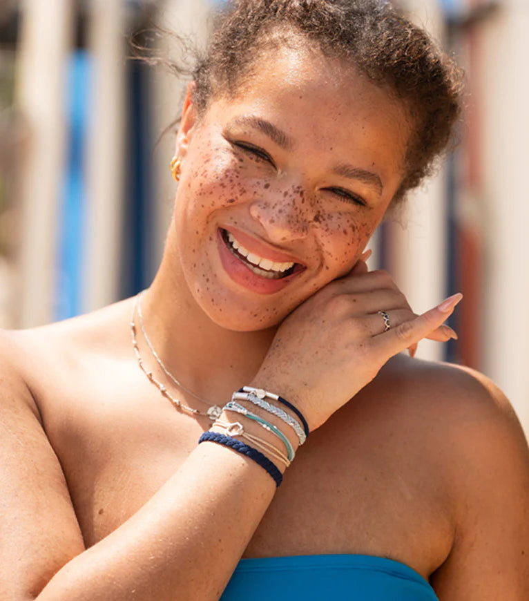 Woman with freckles wearing multiple bracelets on a blurred outdoor background