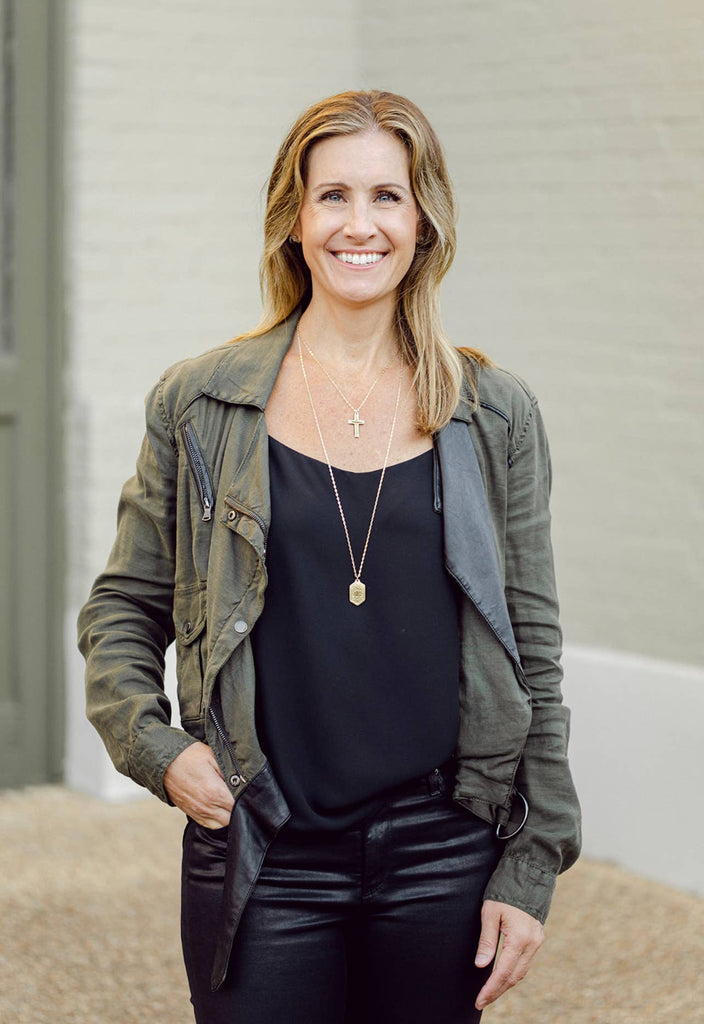 person wearing multiple necklaces in front of a distant brick wall