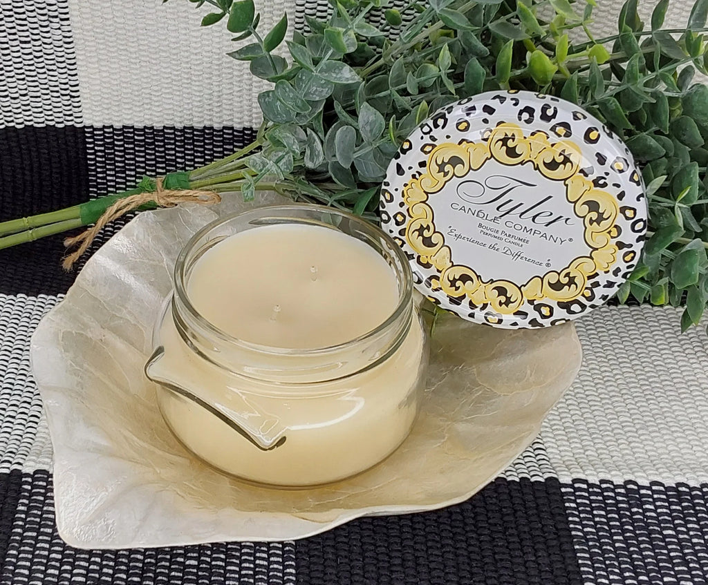 candle on a cream leaf on a black and white plaid table cloth with a green plant behind it