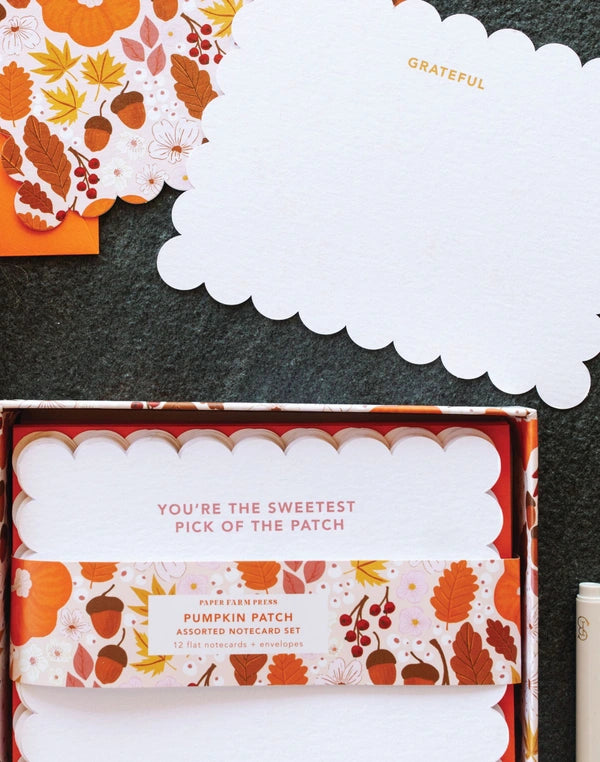 Box of pumpkin-themed cards with autumn leaves and 'Grateful' card on a dark surface
