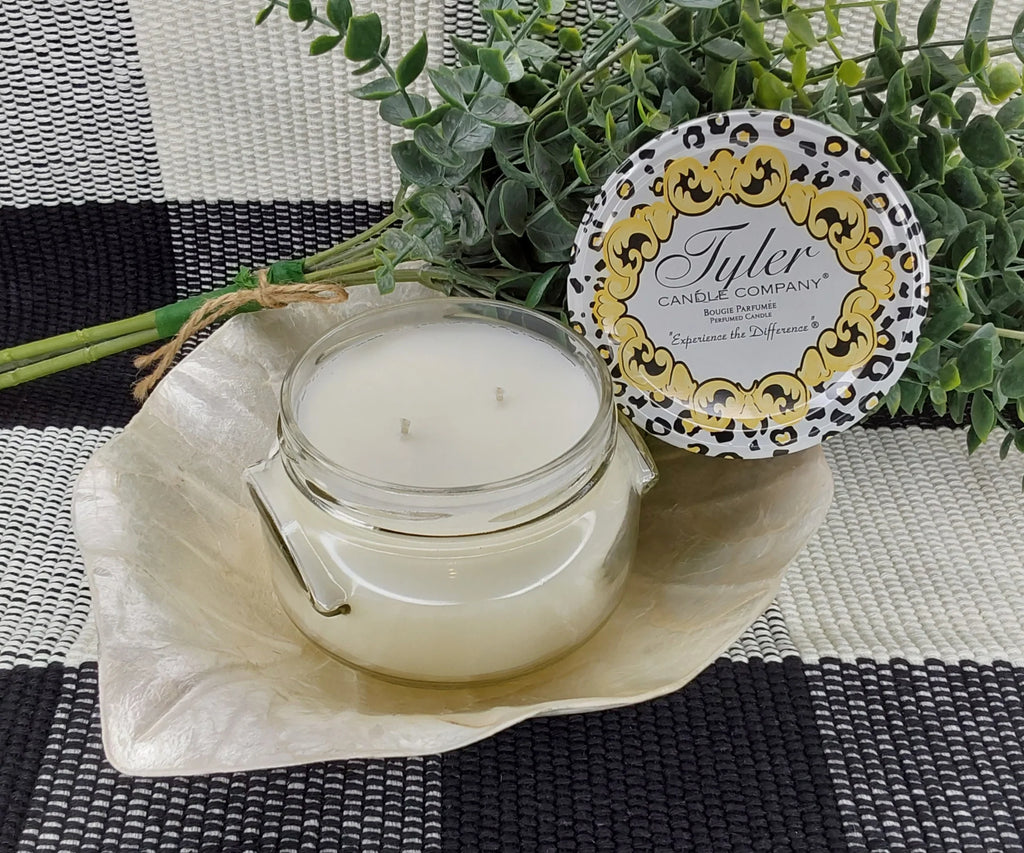 Tyler candle company candle on a white leaf on a black and white plaid table cloth with a green plant behind it