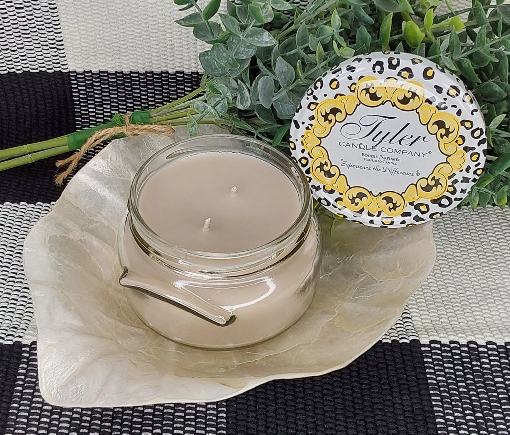 Tyler candle company candle on a white leaf on a black and white plaid table cloth with a green plant behind it