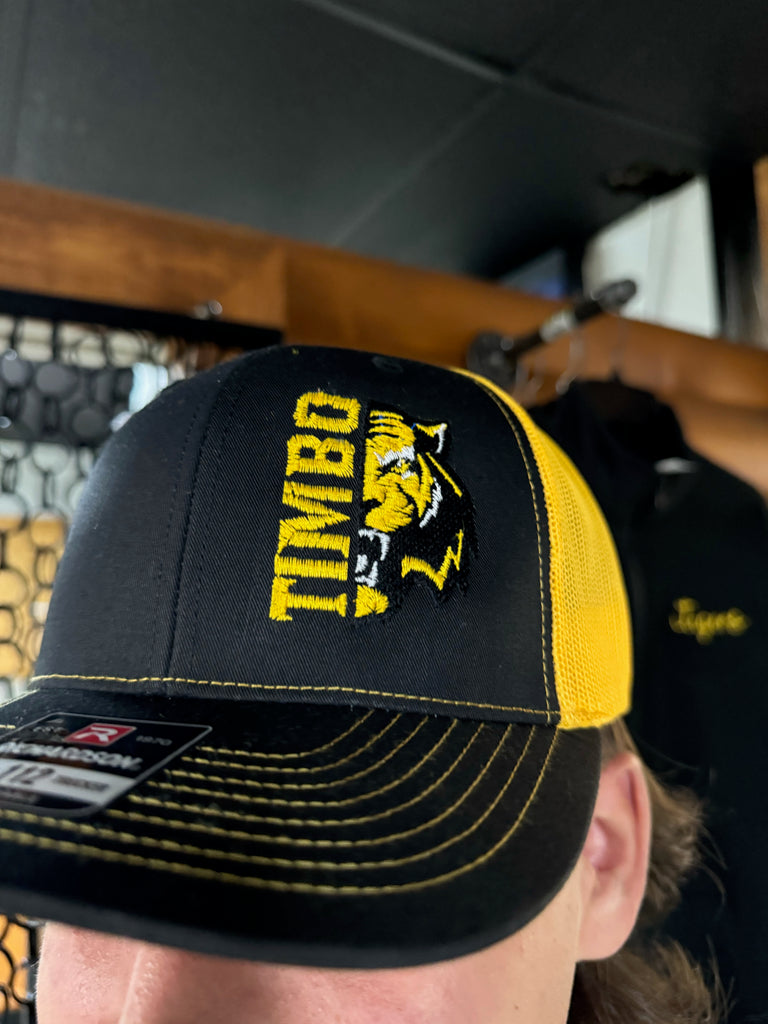 Black cap with yellow logo and text worn by a person sitting in a vehicle.