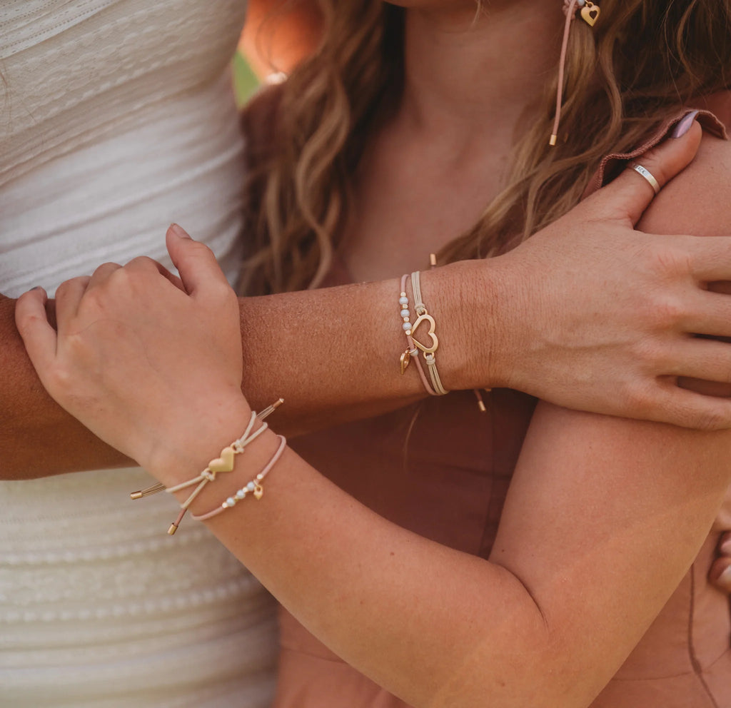 Close-up of two people's arms with gold bracelets on a blurred background
