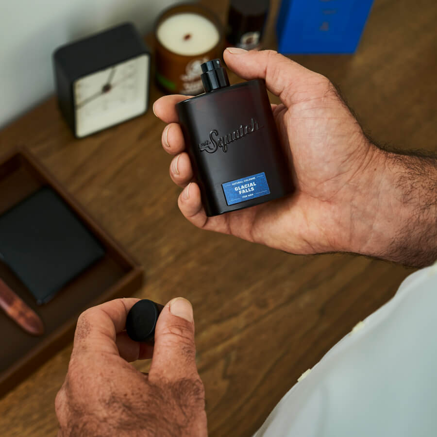 dr squatch glacial falls cologne being held over a wooden table