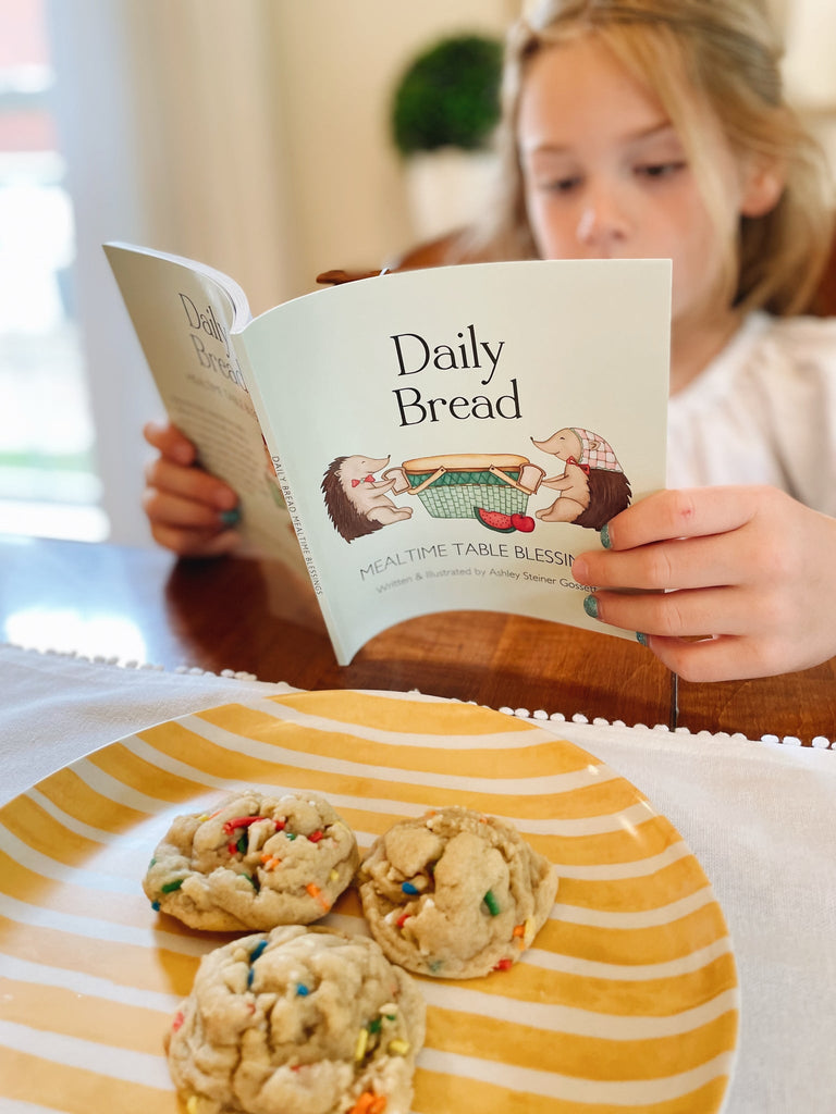 daily bread book being read by a child at dinner table with cookies in front