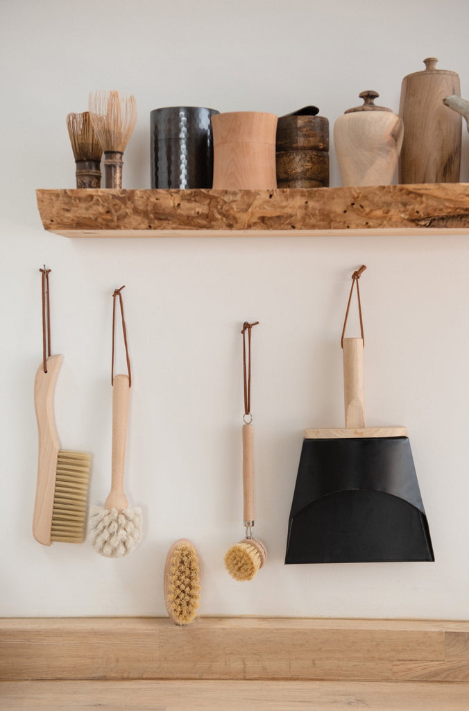 scrubbing tools hanging below a wooden floating shelf on a white wall