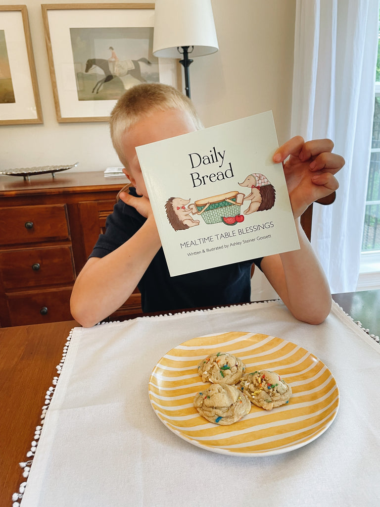 daily bread book being read by a child at dinner table with cookies in front