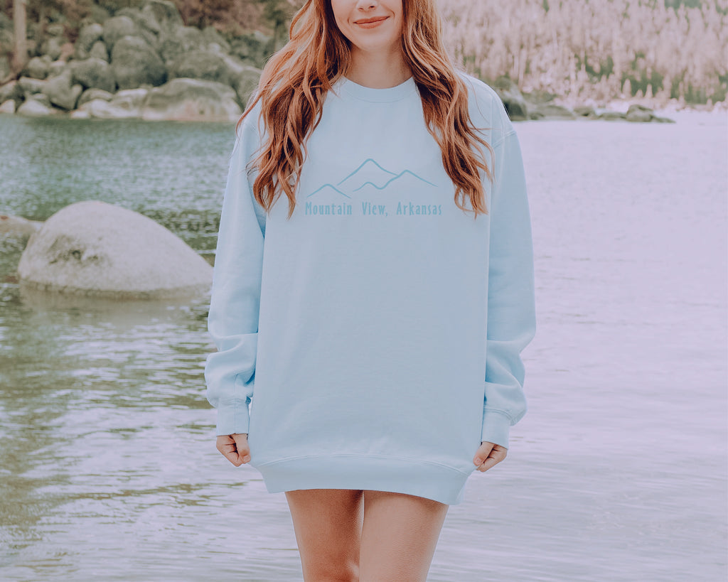 mountain scene embroidery crewneck being worn in front of a lake