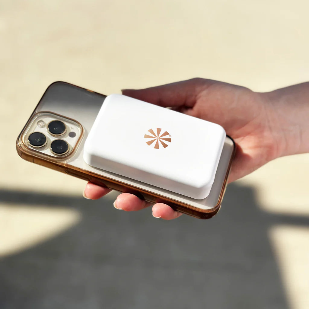 Hand holding a smartphone with a white case featuring a logo on a beige background