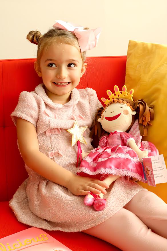 Young girl in a pink dress holding a princess doll on a red couch.