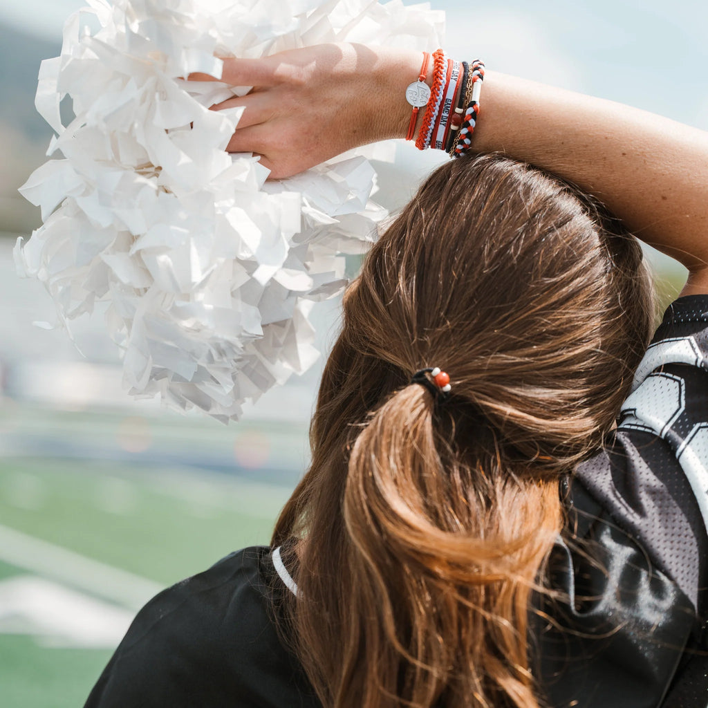 Person holding white pom-poms with a blurred sports field background
