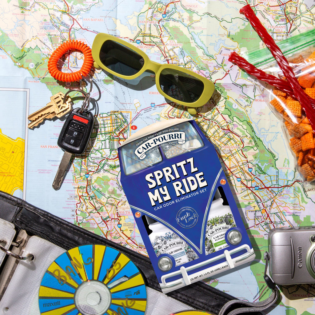 car-pourri odor elimination spray on a map with car keys, sunglasses, a camera, cd, and roadtrip snacks