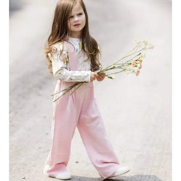 burts bee baby pink overall and floral ruffle shoulder long sleeve shirt on a white background being worn by a child
