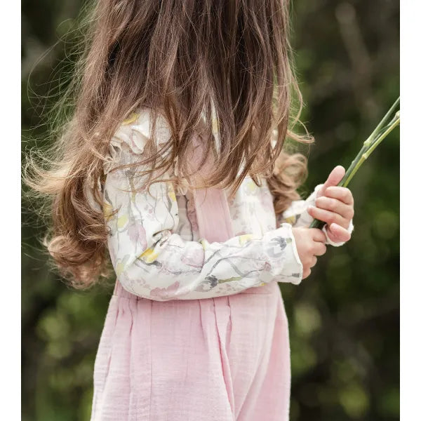 burts bee baby pink overall and floral ruffle shoulder long sleeve shirt on a white background being worn by a child