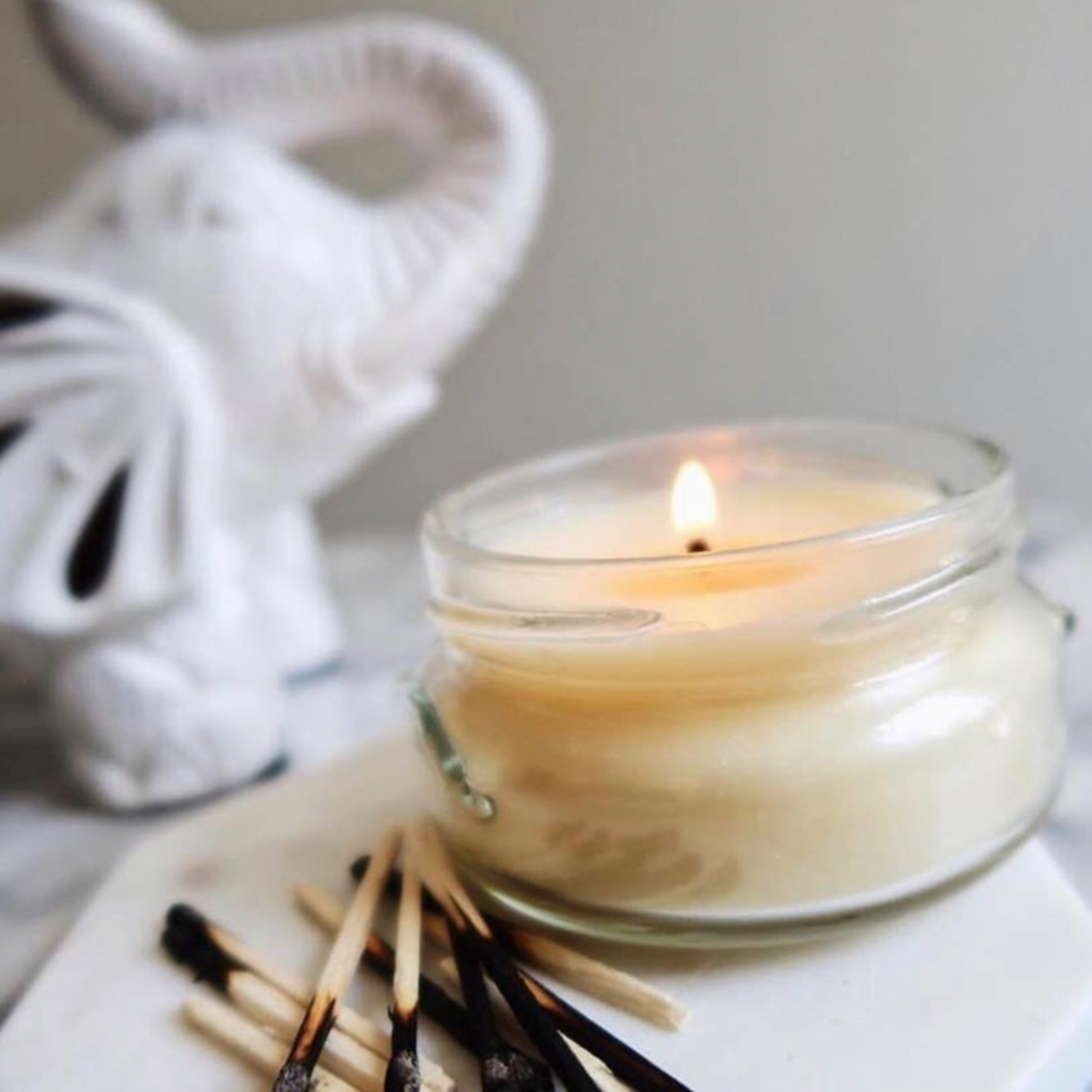 burning candle on a gray background with a white elephant behind it 